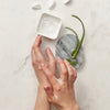 Image of hands applying a clear gel with aloe placed on a stone