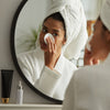 Image of women looking in the mirror and using a cotton pad on her undereye