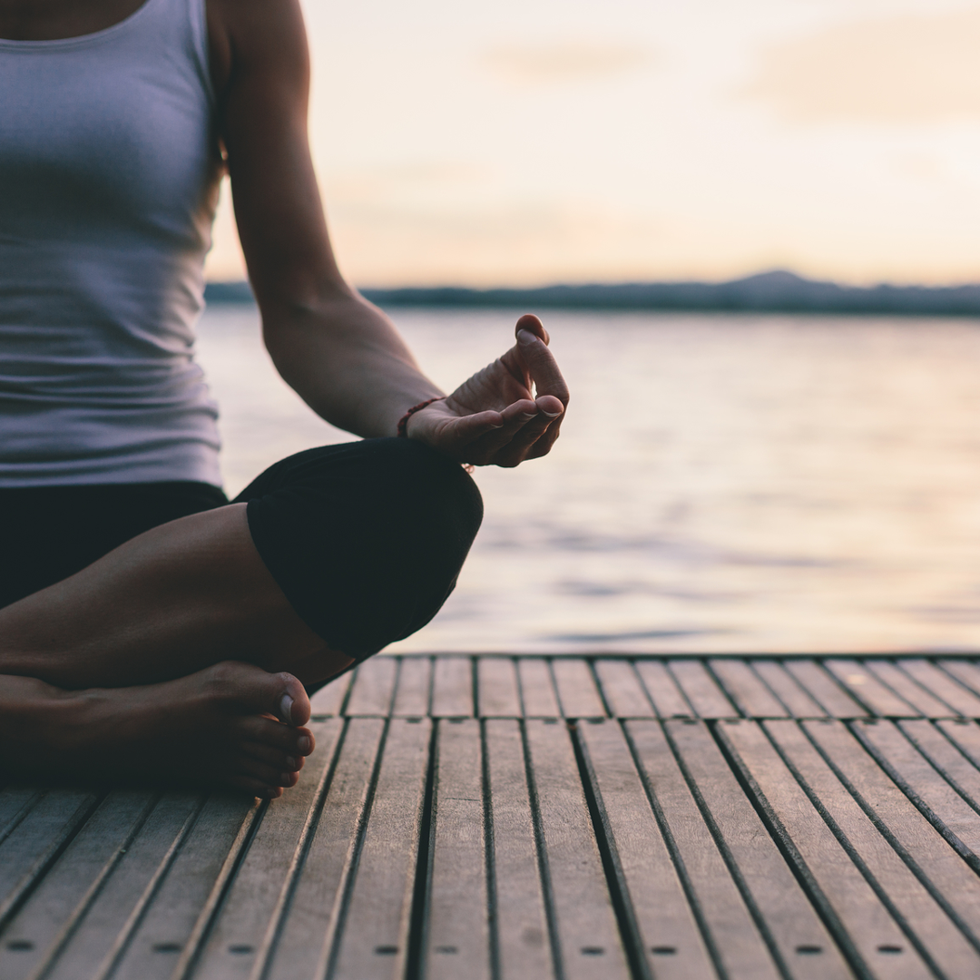 Image of woman sitting on a dock over the water meditating 