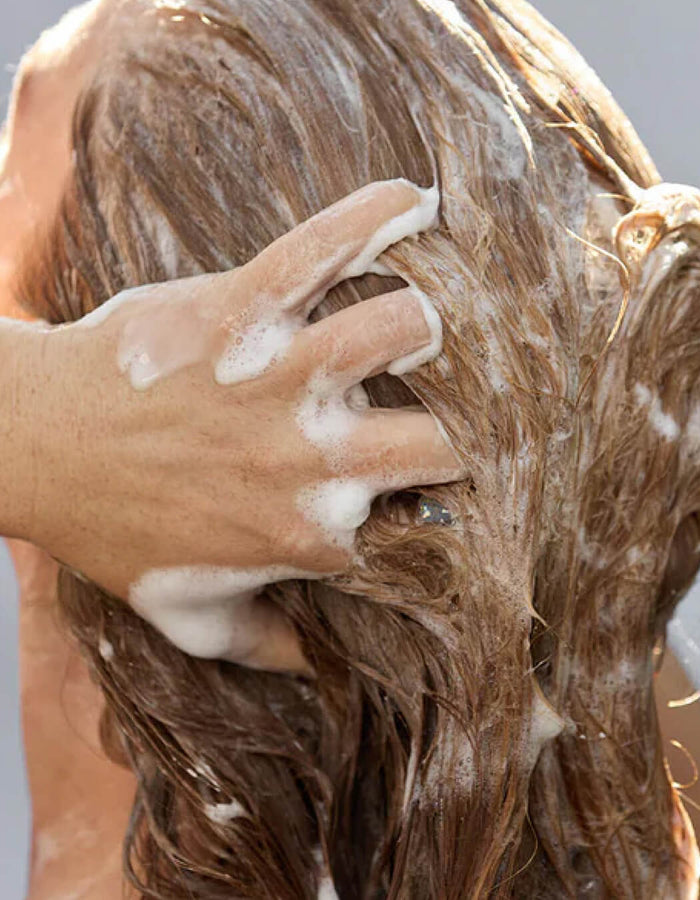 Person washing hair with soapy hands against a neutral background
