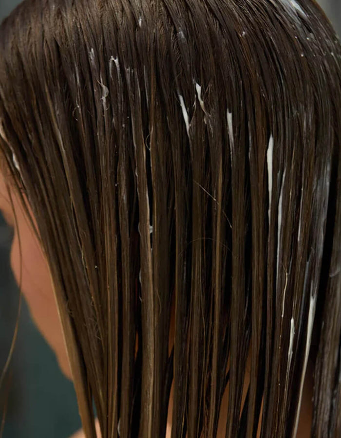 Close-up of wet brown hair with visible product on a blurred background